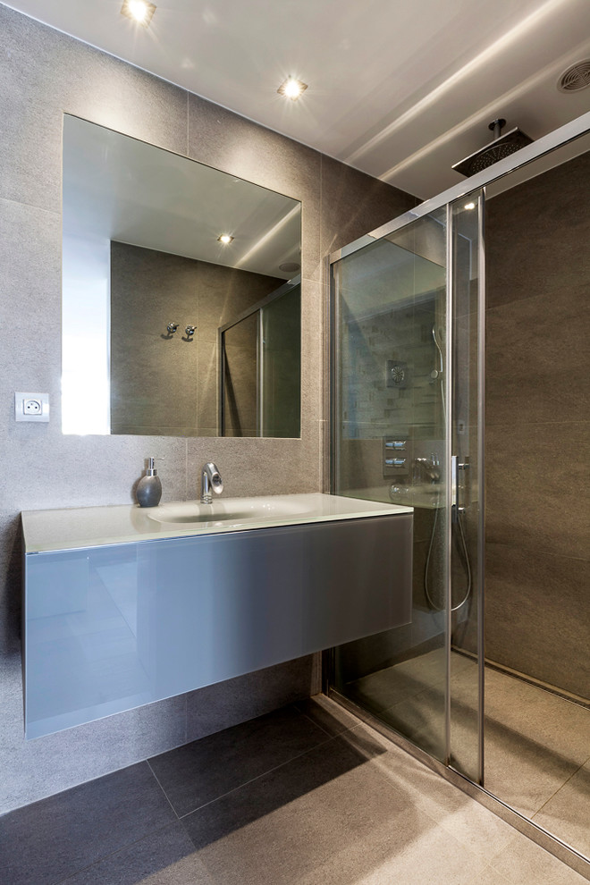 Design ideas for a small contemporary 3/4 bathroom in Paris with a console sink, glass-front cabinets, blue cabinets, glass benchtops, a curbless shower, beige tile, ceramic tile, beige walls and ceramic floors.