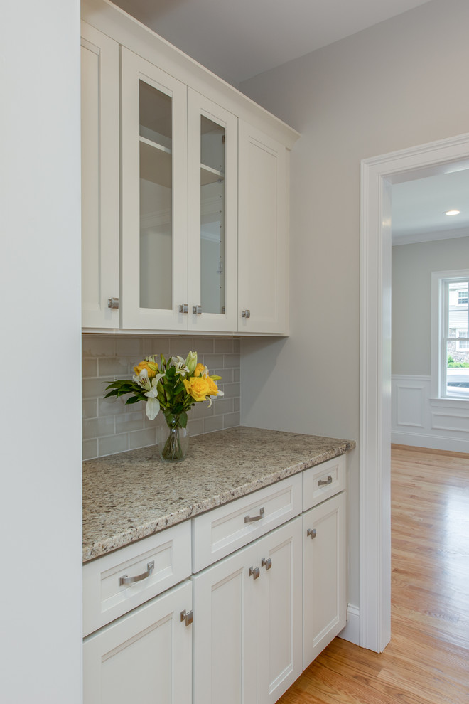 Large transitional l-shaped open plan kitchen in Boston with an undermount sink, shaker cabinets, white cabinets, granite benchtops, grey splashback, subway tile splashback, stainless steel appliances, light hardwood floors and with island.