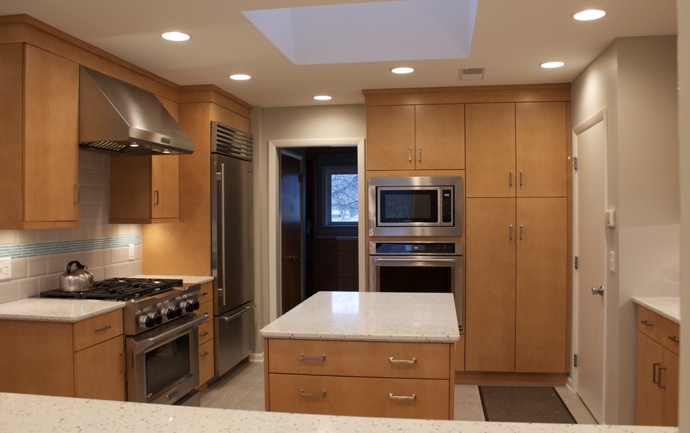 This is an example of a mid-sized contemporary l-shaped eat-in kitchen in Cincinnati with flat-panel cabinets, light wood cabinets, quartz benchtops, ceramic splashback, stainless steel appliances, porcelain floors, with island, an undermount sink and grey splashback.
