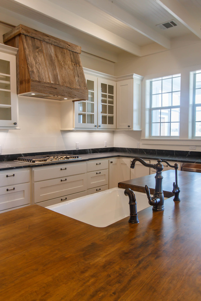 This is an example of a mid-sized country galley open plan kitchen in Houston with a farmhouse sink, shaker cabinets, black cabinets, stainless steel appliances, dark hardwood floors, with island, brown floor and soapstone benchtops.