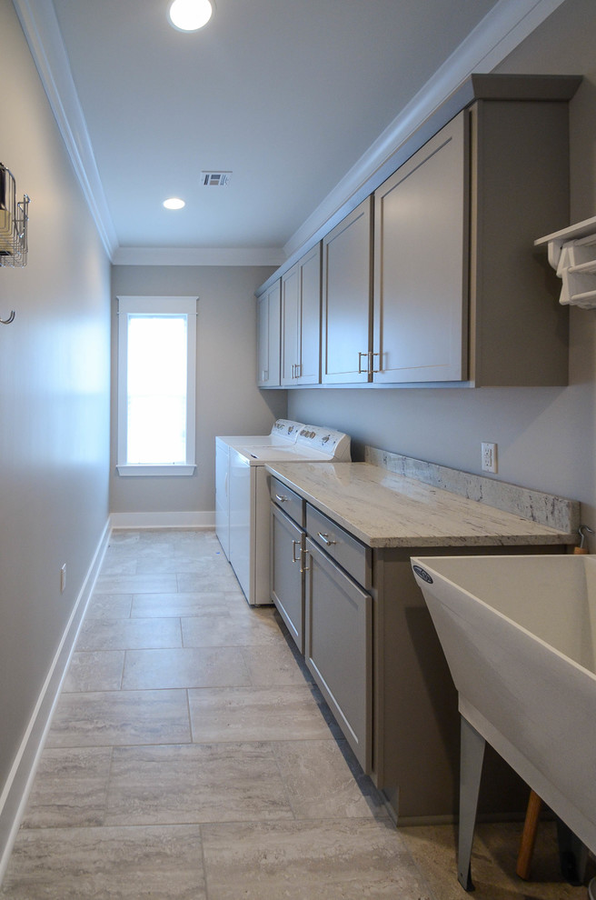 This is an example of a mid-sized traditional galley laundry room in New Orleans with an utility sink, flat-panel cabinets, grey cabinets, granite benchtops, grey walls, ceramic floors and a side-by-side washer and dryer.