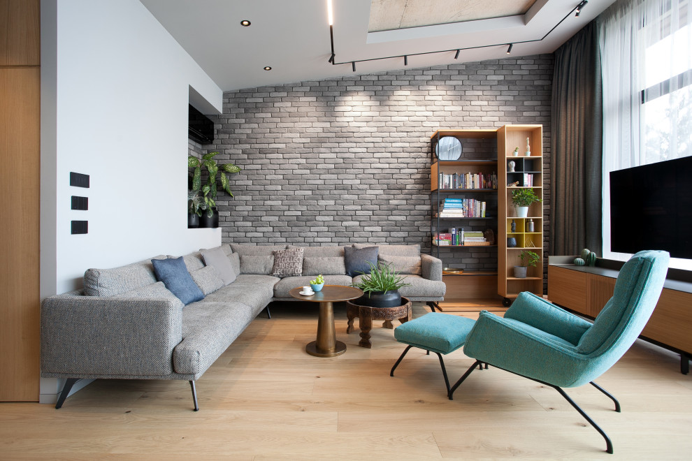 Idée de décoration pour un salon design de taille moyenne et ouvert avec un mur gris, parquet clair, un téléviseur fixé au mur et un mur en parement de brique.