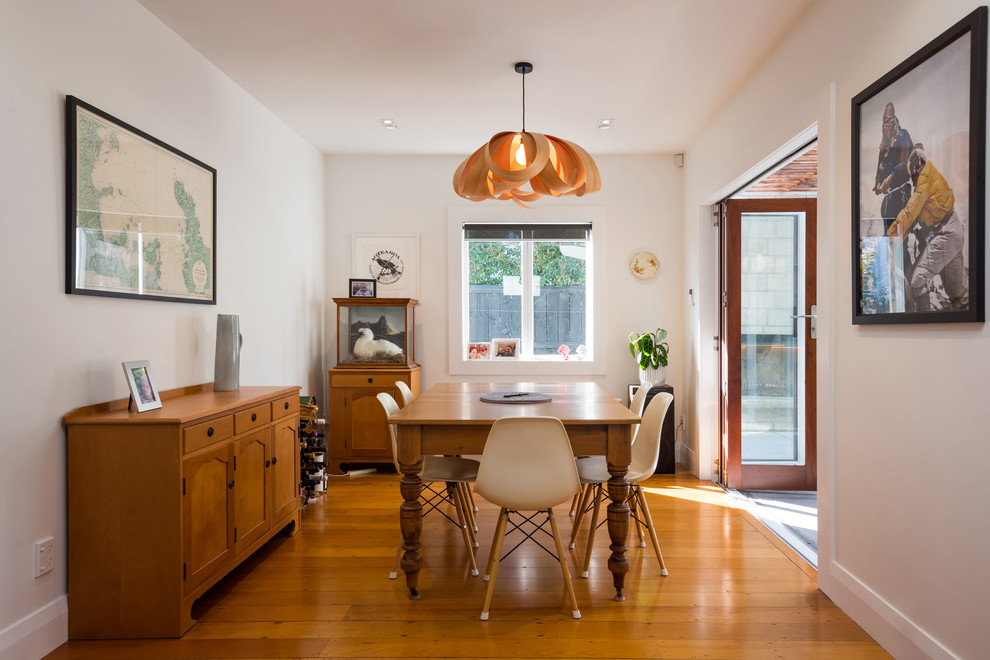 Transitional dining room in Auckland with white walls, medium hardwood floors and brown floor.