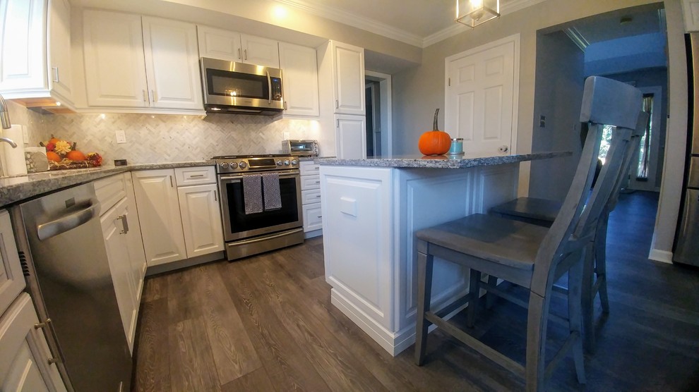 This is an example of a mid-sized transitional l-shaped eat-in kitchen in Philadelphia with an undermount sink, raised-panel cabinets, white cabinets, granite benchtops, grey splashback, mosaic tile splashback, stainless steel appliances, vinyl floors, with island, grey floor and grey benchtop.