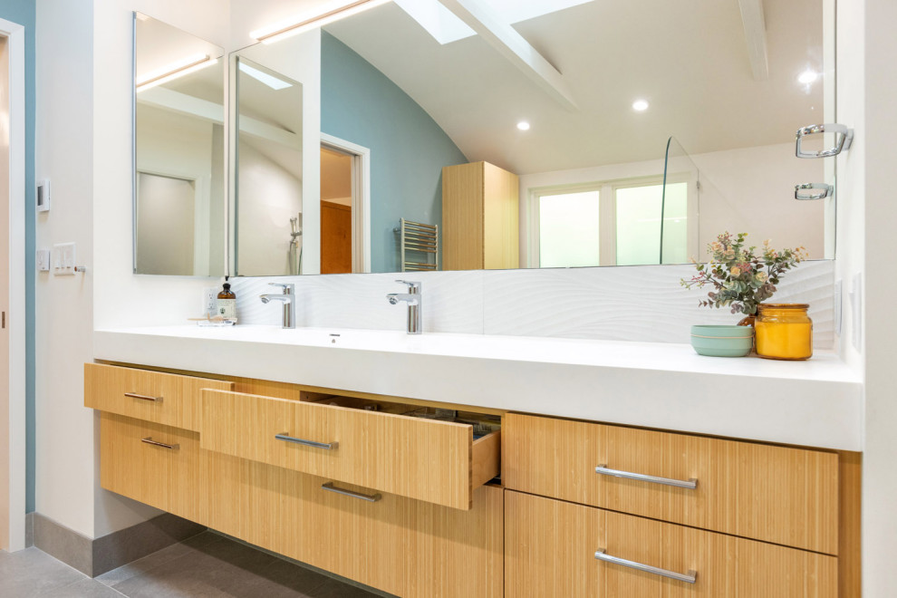 This is an example of a large contemporary master bathroom in San Francisco with flat-panel cabinets, light wood cabinets, a curbless shower, a wall-mount toilet, white tile, ceramic tile, blue walls, ceramic floors, a trough sink, solid surface benchtops, grey floor, an open shower, white benchtops, a shower seat, a double vanity, a floating vanity and exposed beam.