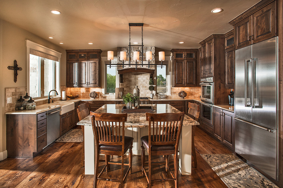 Photo of a traditional u-shaped eat-in kitchen in Denver with a farmhouse sink, raised-panel cabinets, dark wood cabinets, beige splashback, stone tile splashback, stainless steel appliances, dark hardwood floors, with island and brown floor.