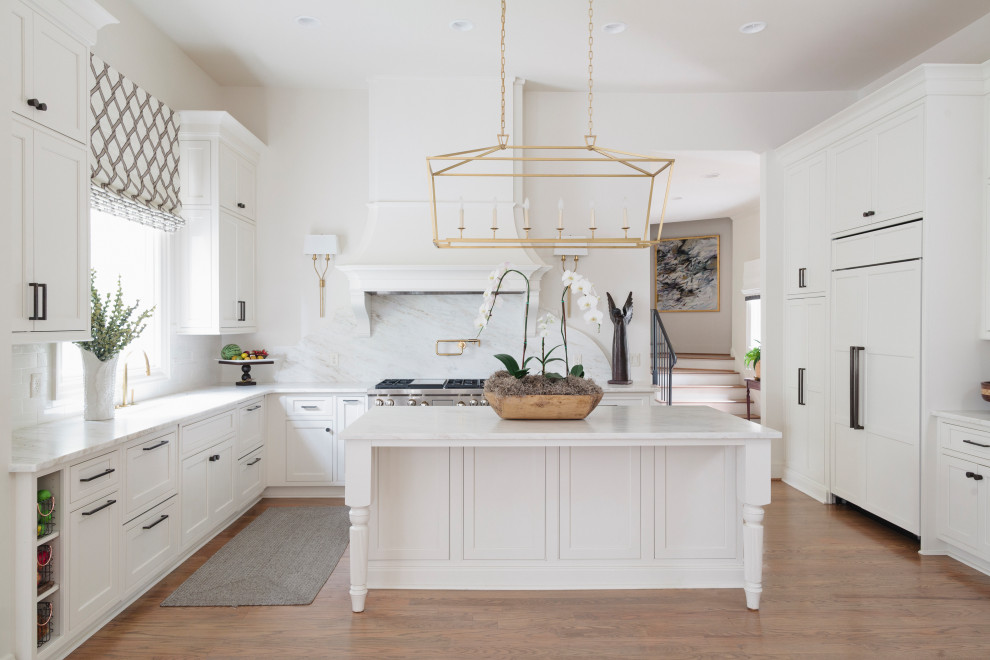 Foto på ett stort funkis vit u-kök, med en dubbel diskho, luckor med infälld panel, vita skåp, integrerade vitvaror, målat trägolv och en köksö