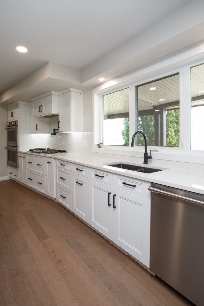 Photo of an expansive transitional l-shaped eat-in kitchen in Calgary with an undermount sink, recessed-panel cabinets, yellow cabinets, quartz benchtops, white splashback, subway tile splashback, stainless steel appliances, medium hardwood floors, with island, brown floor, white benchtop and exposed beam.