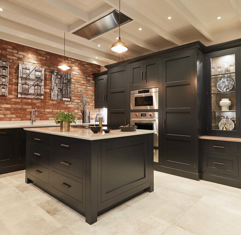 Inspiration for a large transitional u-shaped eat-in kitchen in Cambridgeshire with a double-bowl sink, black cabinets, quartzite benchtops, brick splashback, stainless steel appliances, ceramic floors, with island and white benchtop.