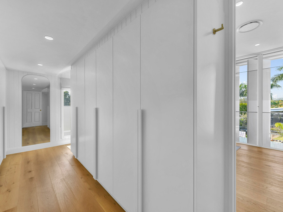 Photo of a scandinavian gender-neutral storage and wardrobe in Brisbane with white cabinets and light hardwood floors.