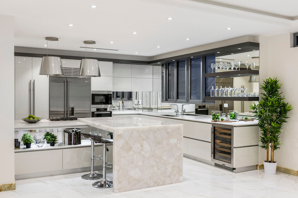 Photo of a contemporary l-shaped open plan kitchen in Brisbane with an undermount sink, flat-panel cabinets, white cabinets, quartz benchtops, metallic splashback, mirror splashback, stainless steel appliances, marble floors and with island.