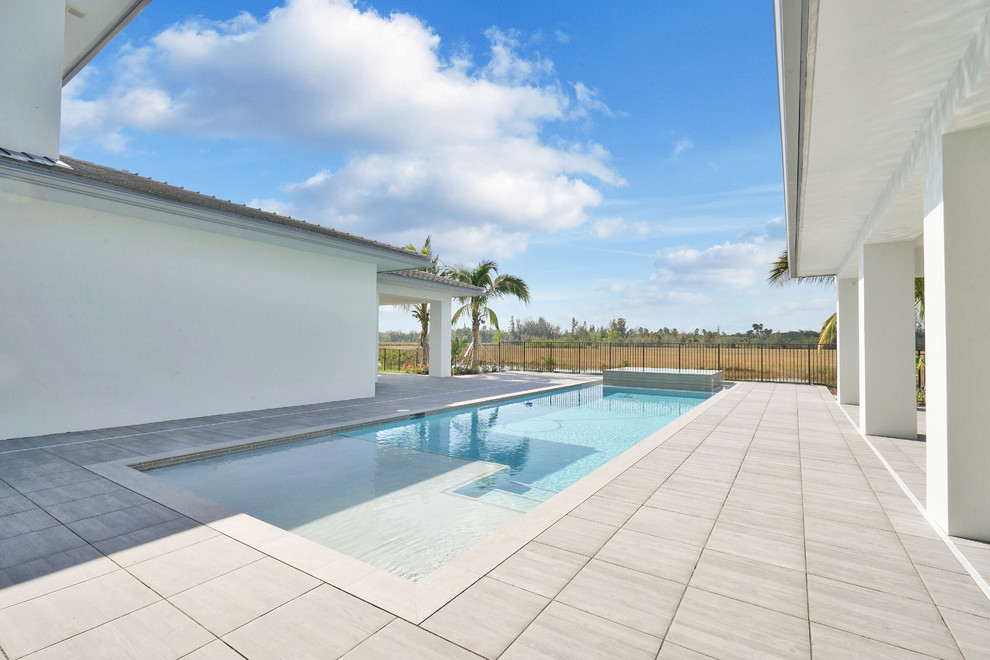 Photo of a mid-sized modern backyard rectangular lap pool in Miami with natural stone pavers and a hot tub.
