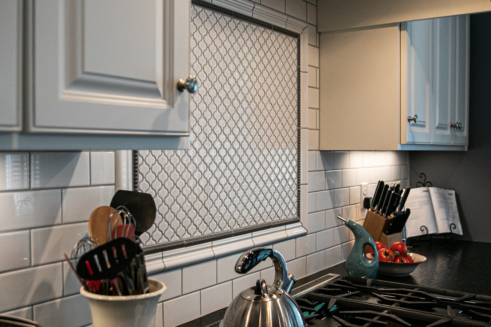 Example of a large transitional l-shaped medium tone wood floor and brown floor open concept kitchen design in Charlotte with a farmhouse sink, white cabinets, granite countertops, white backsplash, stainless steel appliances, an island, raised-panel cabinets, porcelain backsplash and white countertops