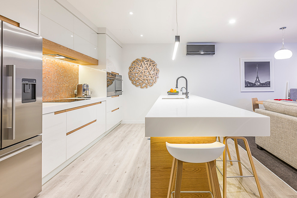 Design ideas for a mid-sized contemporary galley eat-in kitchen in Auckland with an undermount sink, white cabinets, orange splashback, mosaic tile splashback, stainless steel appliances, flat-panel cabinets, a peninsula, solid surface benchtops, light hardwood floors and multi-coloured floor.