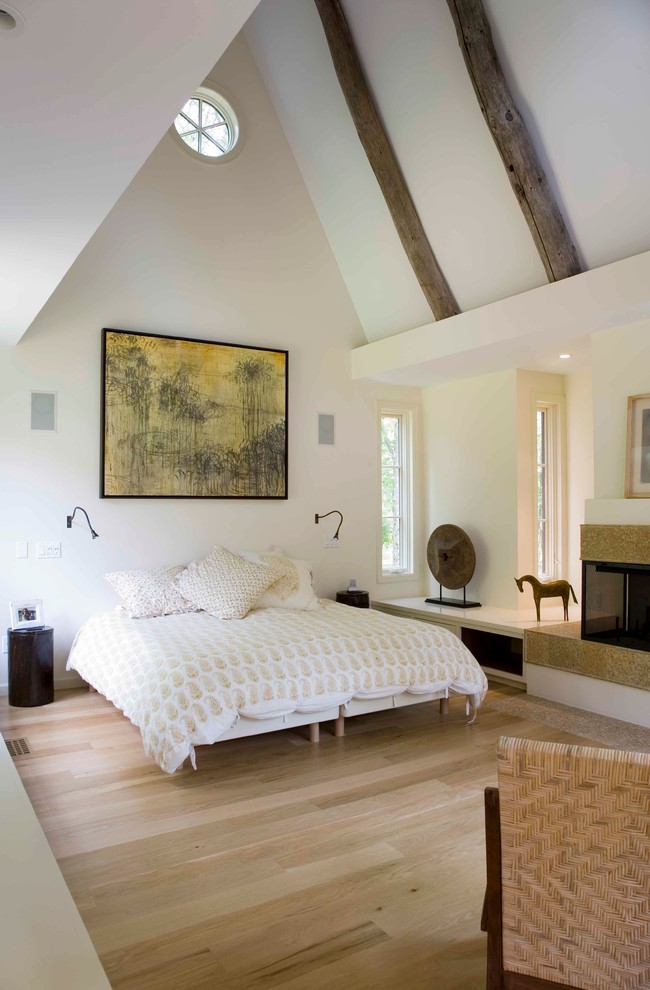 Photo of a transitional master bedroom in New York with beige walls, light hardwood floors and a corner fireplace.