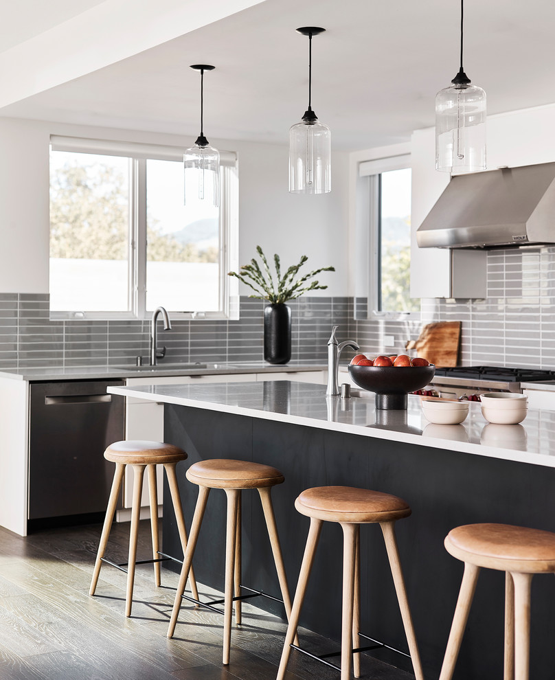 Inspiration for a contemporary l-shaped kitchen in San Francisco with an undermount sink, flat-panel cabinets, white cabinets, grey splashback, glass tile splashback, stainless steel appliances, dark hardwood floors, with island, brown floor and grey benchtop.