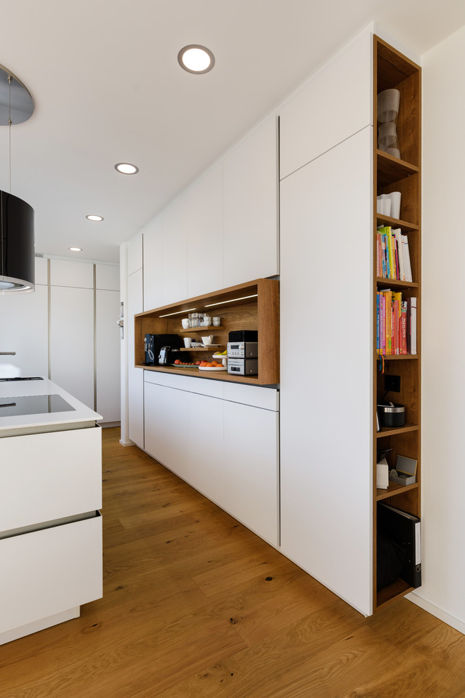 Design ideas for a mid-sized contemporary l-shaped open plan kitchen in Stuttgart with an integrated sink, flat-panel cabinets, white cabinets, solid surface benchtops, white splashback, timber splashback, black appliances, painted wood floors, with island and brown floor.