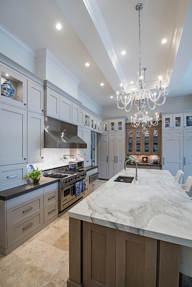 Inspiration for a large transitional l-shaped eat-in kitchen in Miami with stainless steel appliances, with island, shaker cabinets, marble benchtops, grey splashback, stone slab splashback, travertine floors, grey cabinets and an undermount sink.