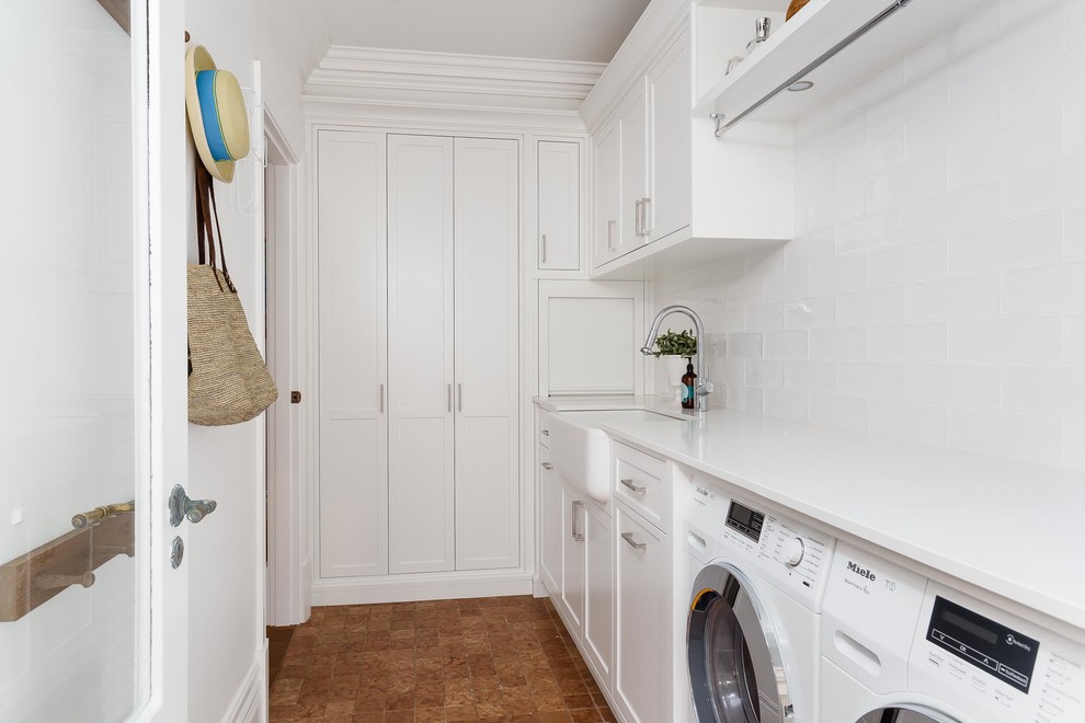 Inspiration for a mid-sized traditional l-shaped laundry room in Perth with a farmhouse sink, shaker cabinets, white cabinets, solid surface benchtops, white walls, porcelain floors, a side-by-side washer and dryer and brown floor.