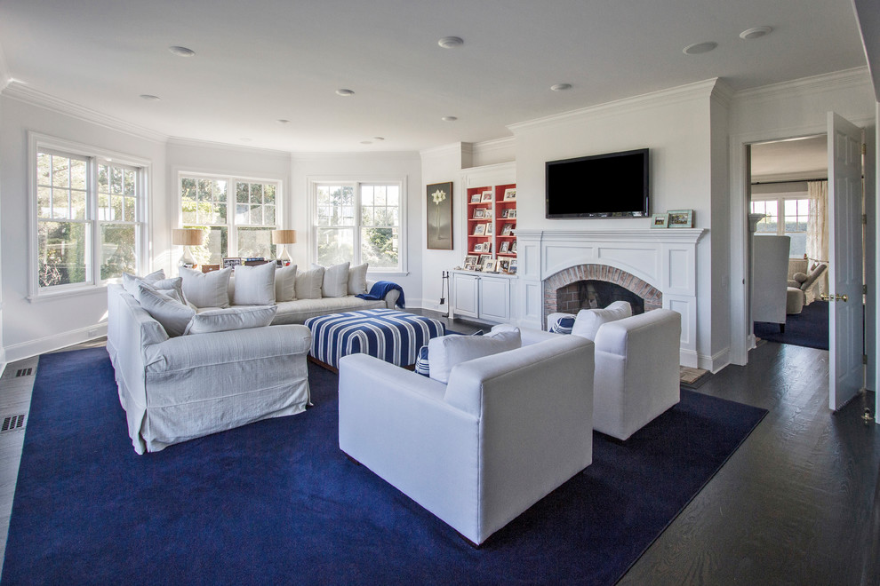Inspiration for a mid-sized beach style enclosed family room in New York with white walls, dark hardwood floors, a standard fireplace, a wood fireplace surround and a wall-mounted tv.