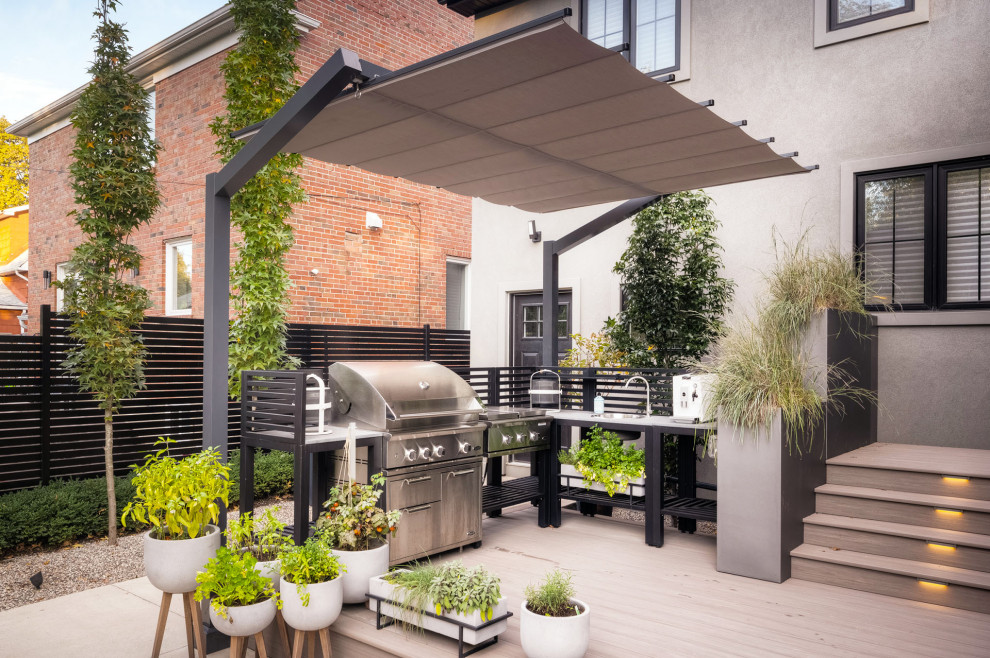 Small transitional backyard and ground level deck in Toronto with an awning and wood railing.