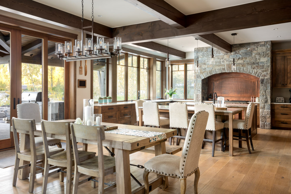 Example of a large mountain style exposed beam, medium tone wood floor and brown floor kitchen/dining room combo design with shaker cabinets, medium tone wood cabinets, granite countertops, two islands, white countertops and white walls