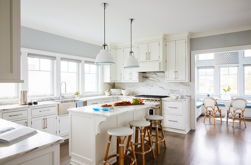 Design ideas for a beach style u-shaped eat-in kitchen in New York with a farmhouse sink, shaker cabinets, white cabinets, white splashback, stainless steel appliances, medium hardwood floors and with island.