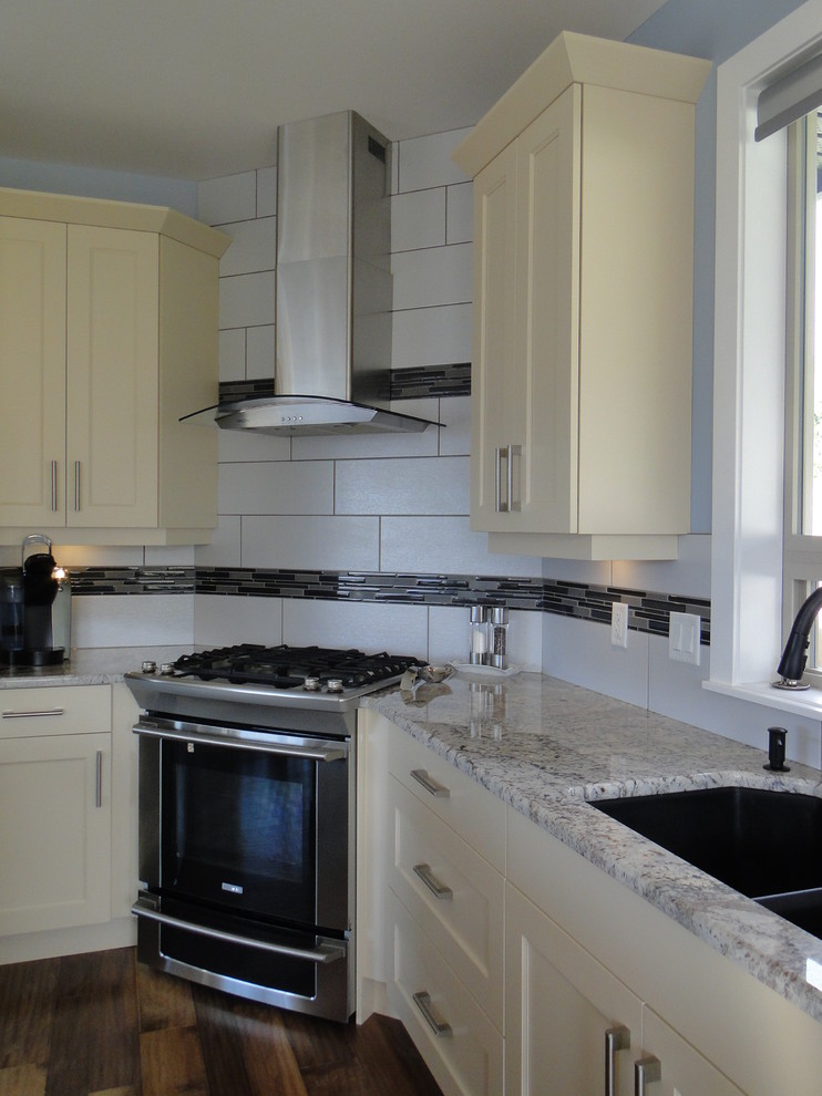 Example of a large transitional l-shaped medium tone wood floor open concept kitchen design in Vancouver with an undermount sink, shaker cabinets, white cabinets, granite countertops, white backsplash, ceramic backsplash, stainless steel appliances and an island