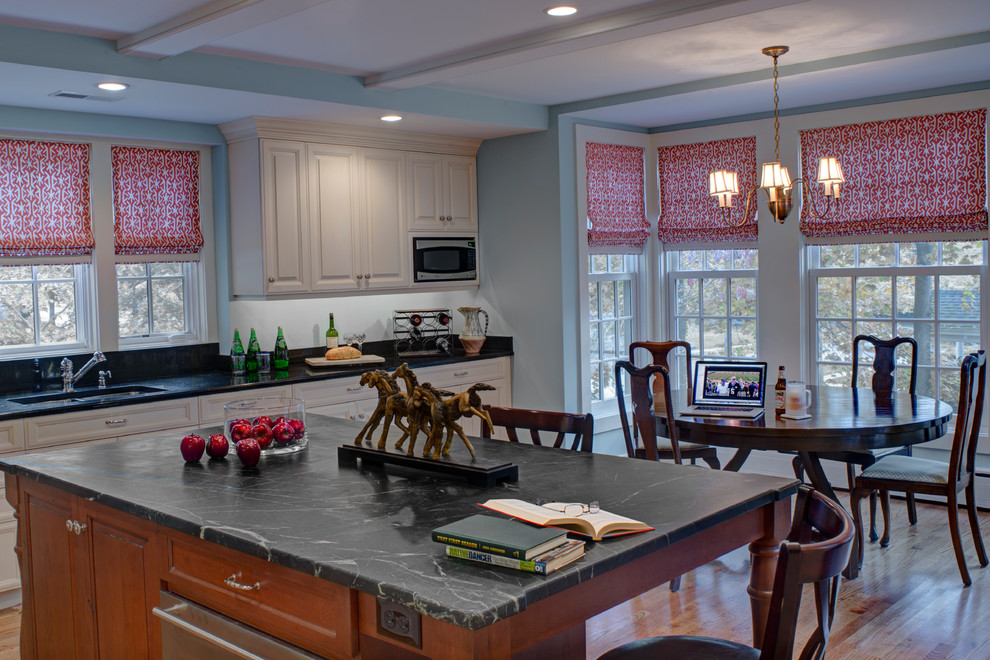 Mid-sized traditional u-shaped eat-in kitchen in Baltimore with an undermount sink, soapstone benchtops, stainless steel appliances, raised-panel cabinets, white cabinets, medium hardwood floors, with island, brown floor and black benchtop.