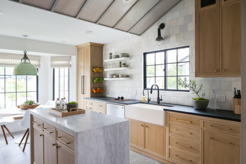Bright modern kitchen with natural wood kitchen cabinets, black countertops, farmhouse sink, and a marble island next to large windows.