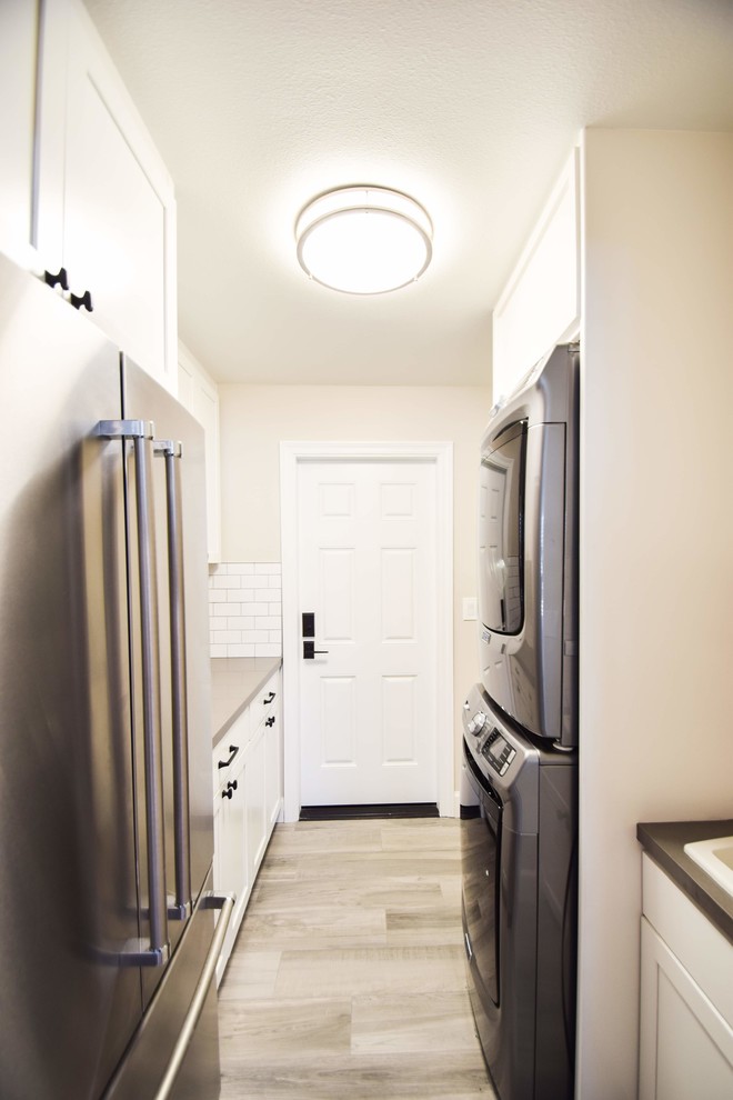 Inspiration for a small transitional galley dedicated laundry room in Los Angeles with shaker cabinets, white cabinets, quartz benchtops, white splashback, glass tile splashback, porcelain floors, grey floor, a drop-in sink, grey walls, a stacked washer and dryer and grey benchtop.