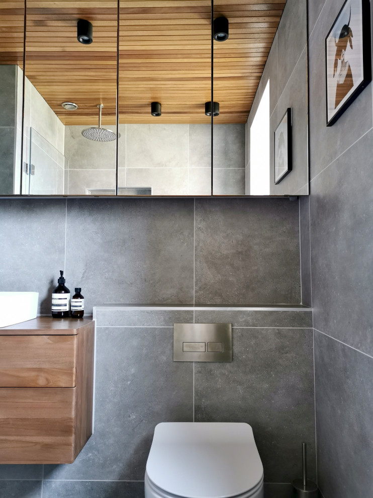 Inspiration for a small contemporary grey and brown bathroom in Other with flat-panel cabinets, brown cabinets, a built-in bath, a shower/bath combination, a wall mounted toilet, grey tiles, porcelain tiles, grey walls, porcelain flooring, grey floors, a single sink, a floating vanity unit and a timber clad ceiling.