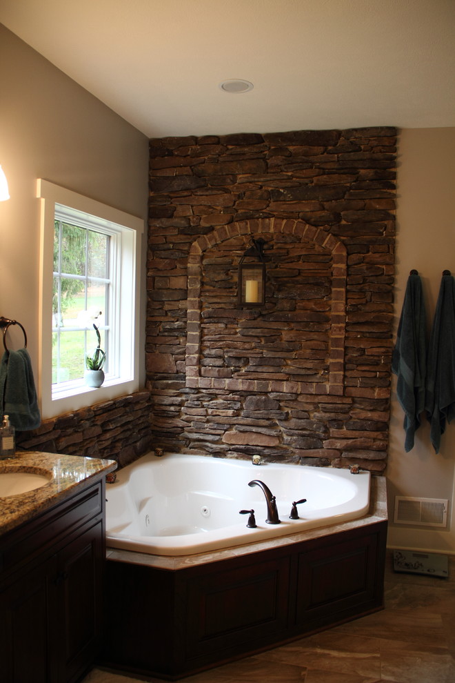 Example of a mid-sized mountain style master brown tile and stone tile medium tone wood floor corner bathtub design with raised-panel cabinets, dark wood cabinets and granite countertops