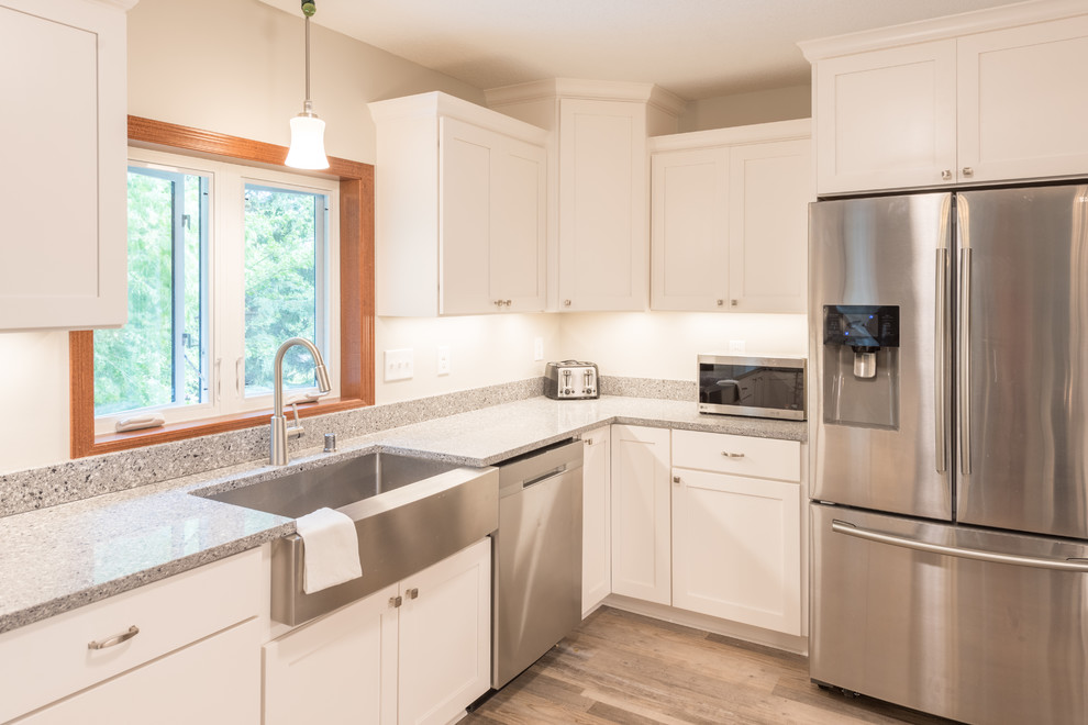 Inspiration for a large transitional u-shaped light wood floor and brown floor enclosed kitchen remodel in Minneapolis with a farmhouse sink, shaker cabinets, white cabinets, granite countertops, stainless steel appliances, a peninsula and gray countertops