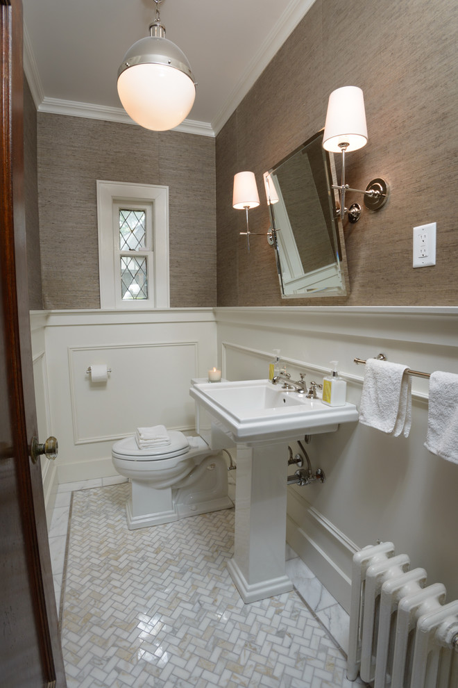 Photo of a mid-sized transitional powder room in New York with a pedestal sink, a two-piece toilet, beige walls and marble floors.