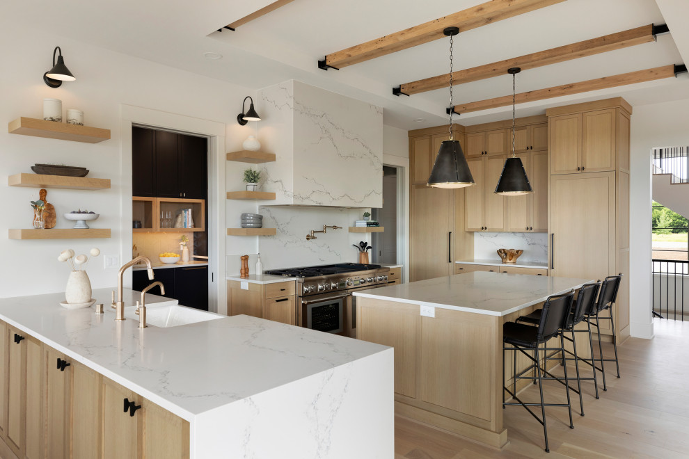 This is an example of a transitional u-shaped kitchen in Minneapolis with an undermount sink, light wood cabinets, quartz benchtops, white splashback, engineered quartz splashback, stainless steel appliances, light hardwood floors, with island, white benchtop and vaulted.
