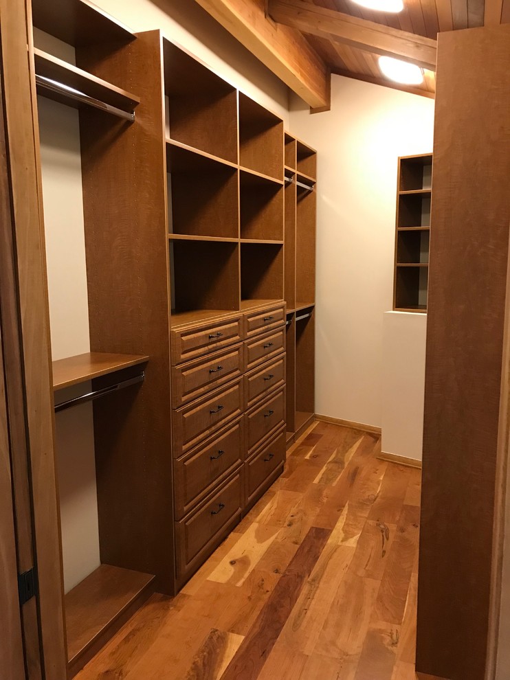 Design ideas for a mid-sized traditional gender-neutral walk-in wardrobe in Other with raised-panel cabinets, medium wood cabinets, medium hardwood floors and brown floor.