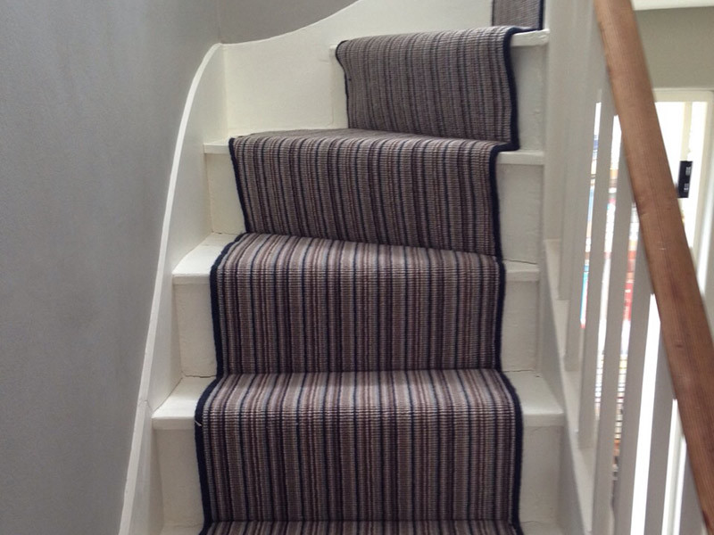 Photo of a mid-sized contemporary carpeted u-shaped staircase in London with carpet risers and wood railing.