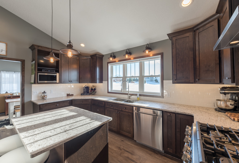 Example of a large mountain style u-shaped dark wood floor and brown floor enclosed kitchen design in Minneapolis with a double-bowl sink, shaker cabinets, dark wood cabinets, granite countertops, white backsplash, subway tile backsplash, stainless steel appliances and an island