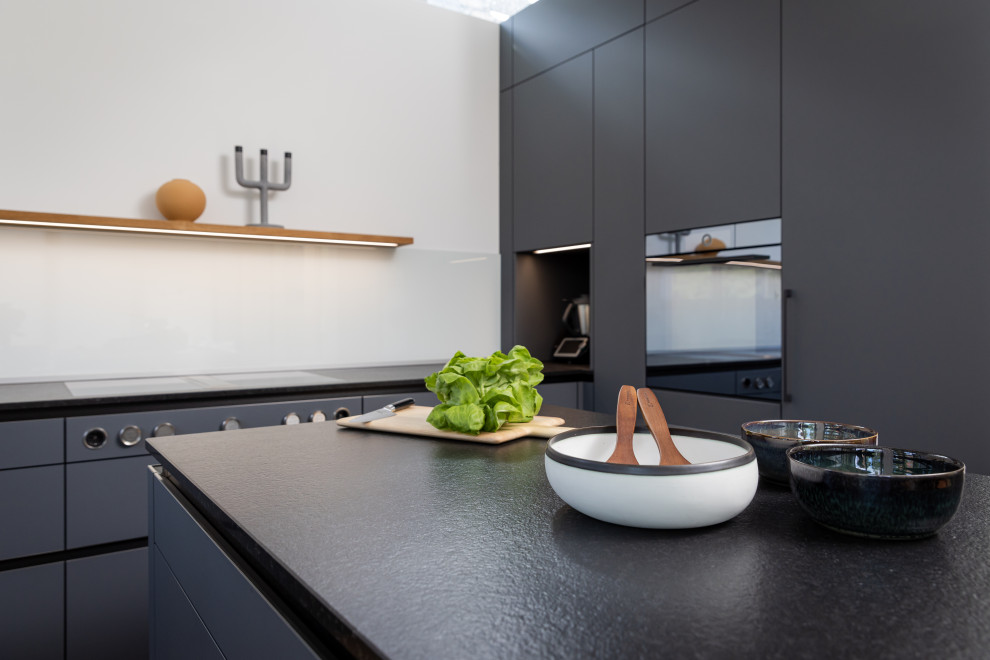 Modern inredning av ett mellanstort, avskilt svart svart l-kök, med släta luckor, grå skåp, granitbänkskiva, svarta vitvaror och en halv köksö