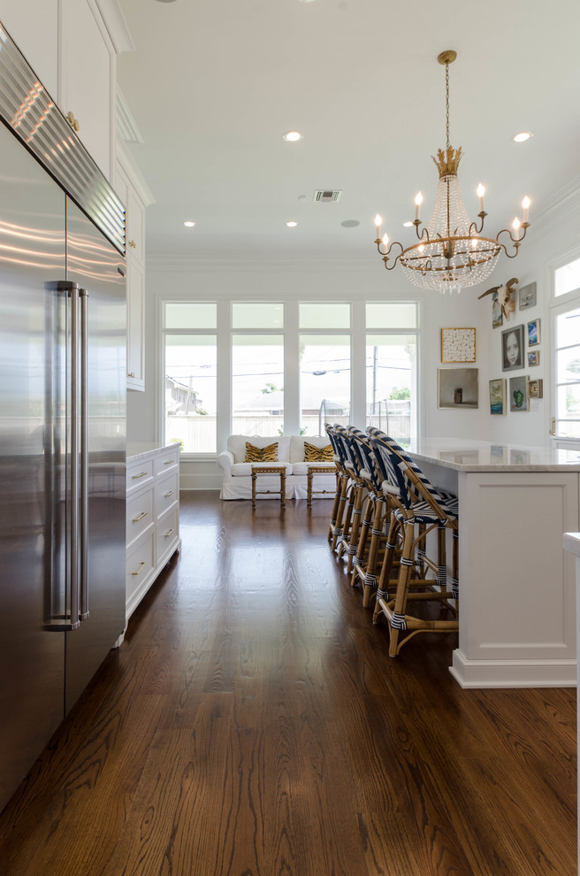 Photo of a mid-sized beach style u-shaped kitchen in New Orleans with a farmhouse sink, raised-panel cabinets, white cabinets, marble benchtops, white splashback, stainless steel appliances, dark hardwood floors and with island.