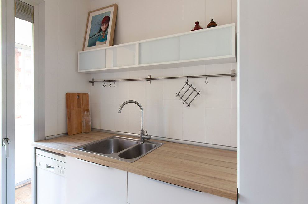 This is an example of a small galley separate kitchen in Barcelona with a double-bowl sink, flat-panel cabinets, white cabinets, laminate benchtops, white splashback, ceramic splashback, stainless steel appliances, linoleum floors and brown floor.