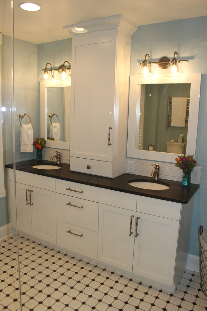 Photo of a large traditional master bathroom in DC Metro with shaker cabinets, white cabinets, a one-piece toilet, white tile, subway tile, blue walls, ceramic floors, an undermount sink, solid surface benchtops, white floor, a hinged shower door and black benchtops.