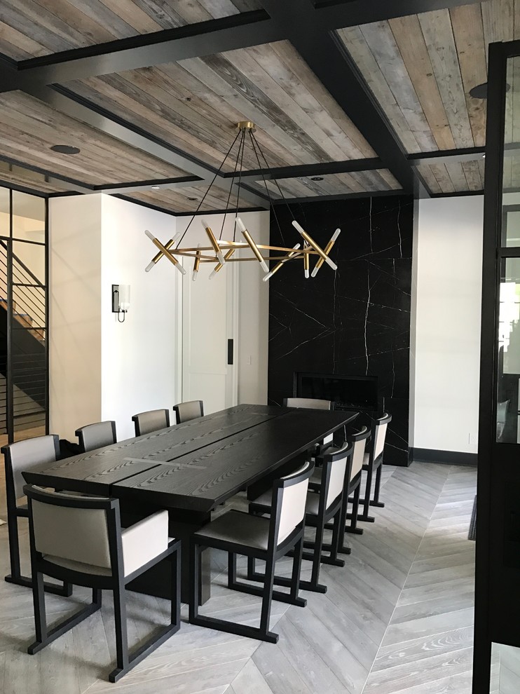 This is an example of an industrial separate dining room in Los Angeles with white walls, a standard fireplace, a stone fireplace surround and grey floor.