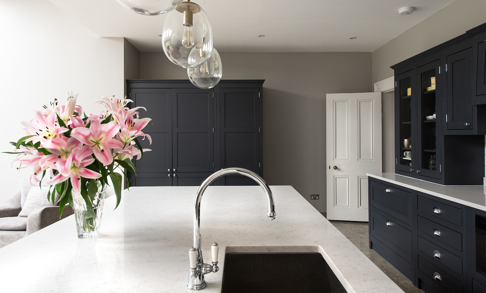 Mid-sized traditional open plan kitchen in London with a drop-in sink, shaker cabinets, dark wood cabinets, marble benchtops, white splashback, ceramic splashback, black appliances and with island.