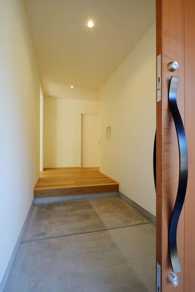 Inredning av en minimalistisk mellanstor hall, med vita väggar, betonggolv, en skjutdörr, mellanmörk trädörr och grått golv