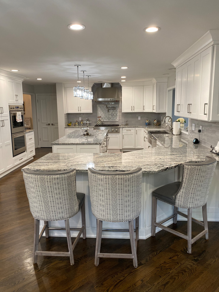 Inspiration for a large transitional u-shaped eat-in kitchen in Detroit with a farmhouse sink, shaker cabinets, white cabinets, granite benchtops, grey splashback, subway tile splashback, stainless steel appliances, dark hardwood floors, with island, brown floor and multi-coloured benchtop.