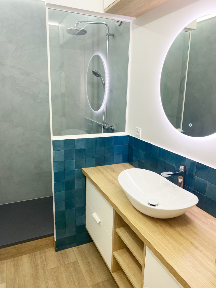 Idéer för att renovera ett mellanstort funkis brun brunt badrum med dusch, med luckor med profilerade fronter, vita skåp, en öppen dusch, en vägghängd toalettstol, blå kakel, vita väggar, ett avlångt handfat, träbänkskiva, brunt golv och med dusch som är öppen