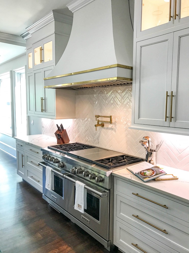 Photo of an expansive transitional kitchen in Charlotte with a farmhouse sink, white cabinets, quartz benchtops, white splashback, ceramic splashback, stainless steel appliances, dark hardwood floors, with island, brown floor, white benchtop and recessed-panel cabinets.