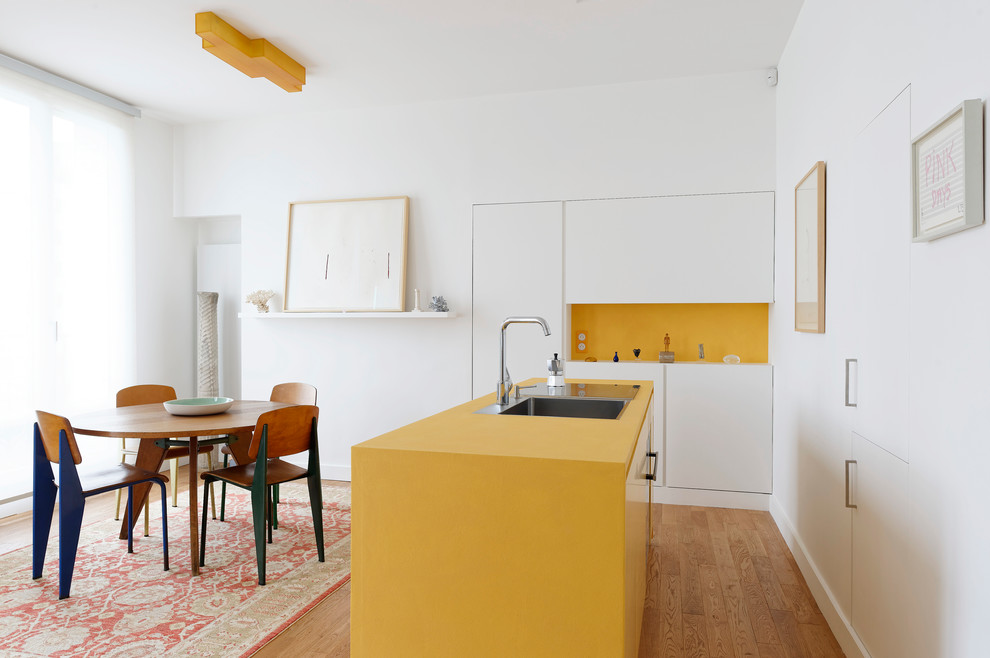 Photo of a small contemporary single-wall eat-in kitchen in Paris with a single-bowl sink, flat-panel cabinets, white cabinets, yellow splashback, light hardwood floors, with island and yellow benchtop.